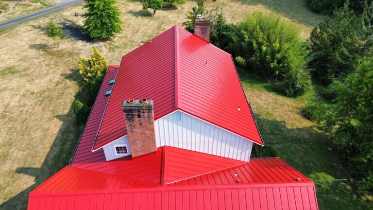 Aerial view of the new red metal roof on a white farmhouse, with a brick chimney and skylights along the lower slope.