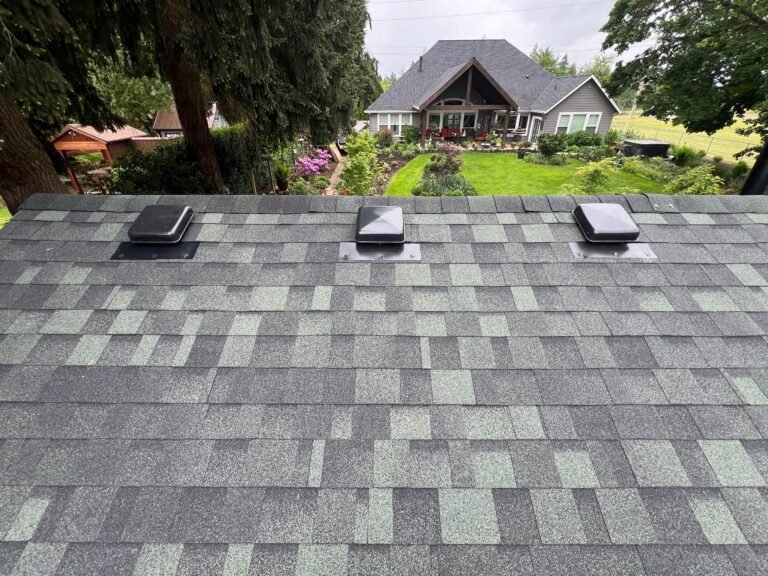 Row of three black box vents on the new shingle roof, with a flower garden and the main house in the distance.