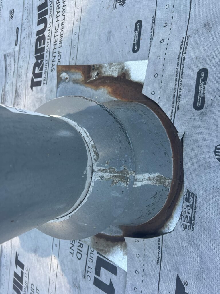 Close-up of a metal vent pipe flashing set into synthetic roofing underlayment, with visible rust at the flange edge.