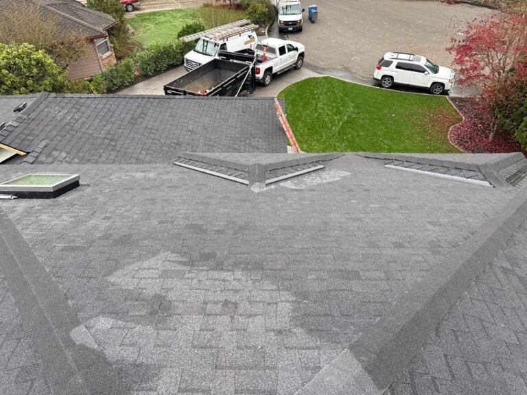 Gray shingle roof in progress with hip lines and a skylight, above a driveway with work trucks, a dump trailer, and a white SUV.