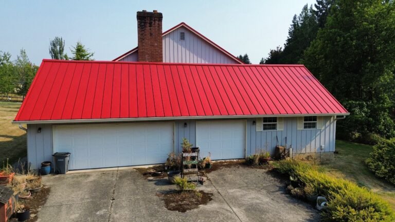 Red metal roof over a three-car garage with white doors, with the brick chimney and upper gable rising behind it.