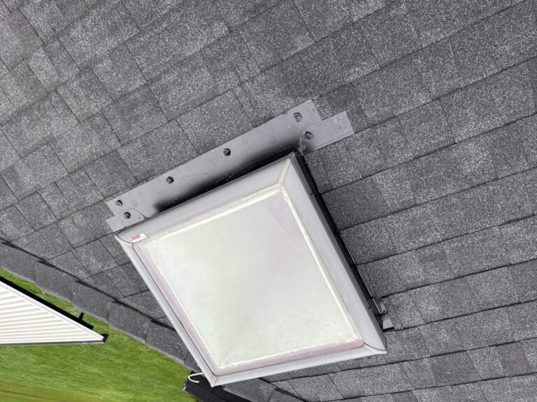 Skylight with a new metal flashing frame set into fresh dark gray shingles.
