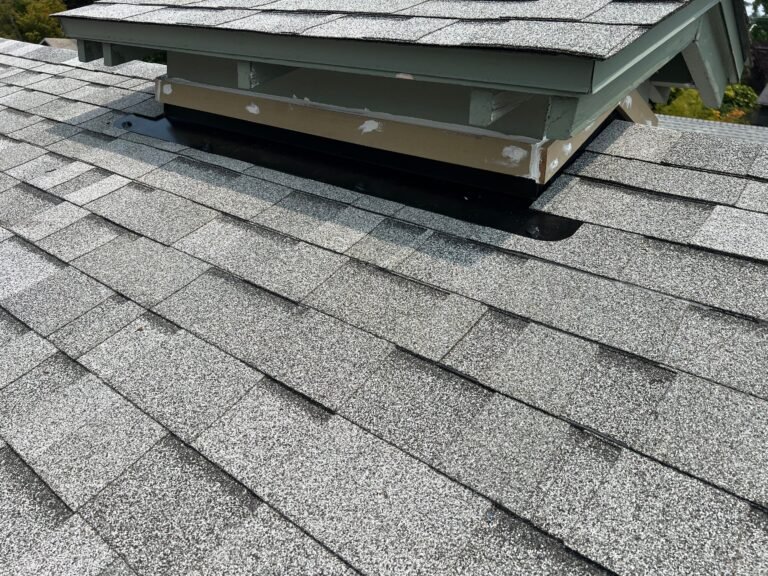 New shingles meeting a green-trimmed roof structure, with black flashing along the base of the wall.
