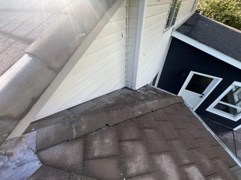 Aged brown shingles meeting a white siding wall, with worn metal step flashing along the joint.