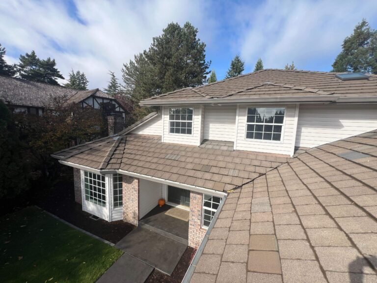 Two-story house with a brick-accented entry and an old brown shingle roof, under a blue sky with clouds.