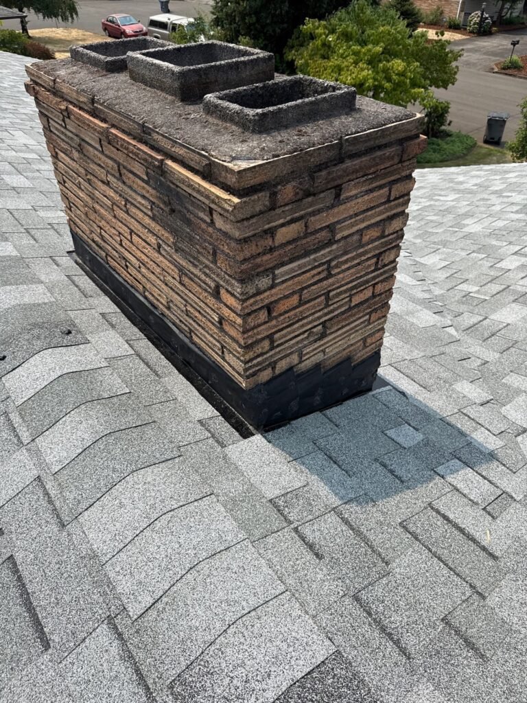 Close-up of the chimney base showing completed black flashing and fresh shingles tucked up against the brick.