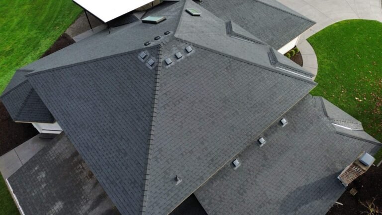 Aerial angle of the finished roof with a prominent hip, vents, and a skylight, beside a white patio cover.
