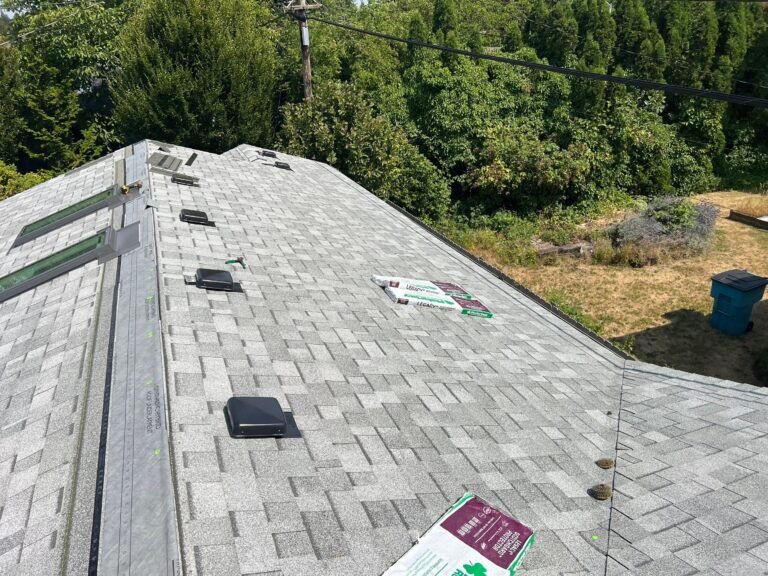 Another angle of the roof in progress, showing skylights, vents, and a shingle bundle near the ridge, over a grassy yard.