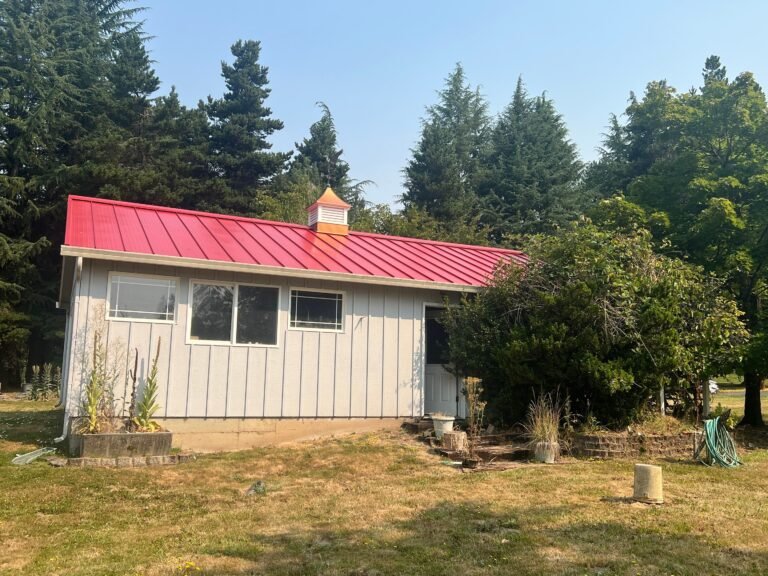 Single-story addition with a new bright red standing seam metal roof, a small cupola on the ridge, and light gray board-and-batten siding.