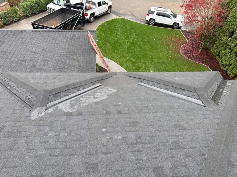 Another view of the roof in progress, showing hip ridge caps and a dump trailer and trucks on the street below.