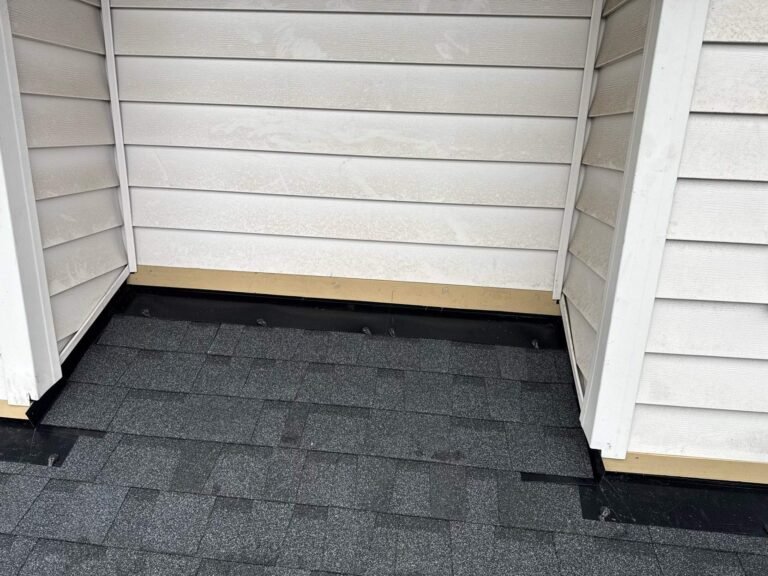 New shingles tucked against a white siding wall with a clean black flashing and trim line at the base.