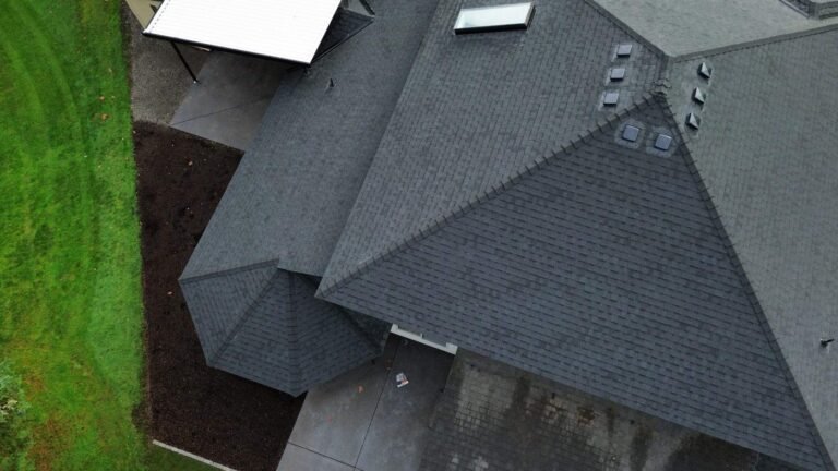 Overhead view of the completed gray roof with multiple hips and valleys, a skylight, and a small group of roof vents.