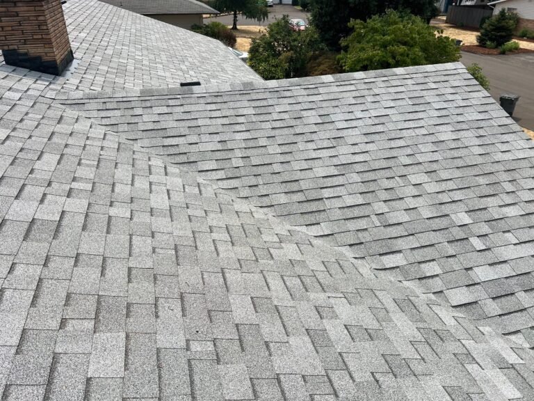 Large completed roof with a clean valley where two shingled slopes meet, and a chimney at the upper left.