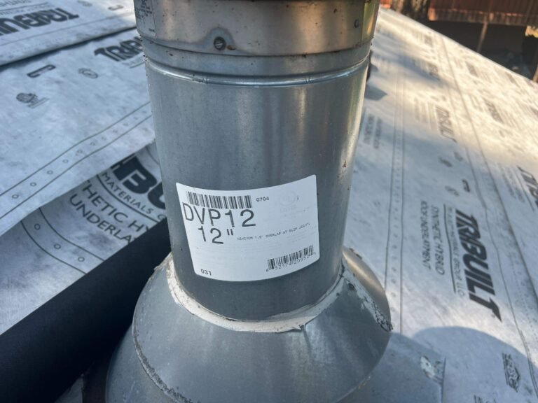 Close-up of a metal vent pipe labeled DVP12 rising through a pipe flashing, surrounded by roofing underlayment.