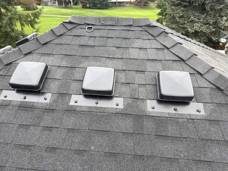 New dark gray shingle roof with three white box vents on metal bases, below a ridge with a golf course beyond.