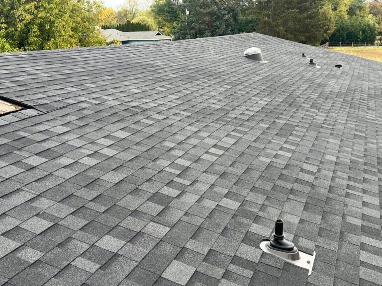 New gray asphalt shingles on a roof slope, with a black plumbing vent pipe boot and a round roof vent near the ridge.