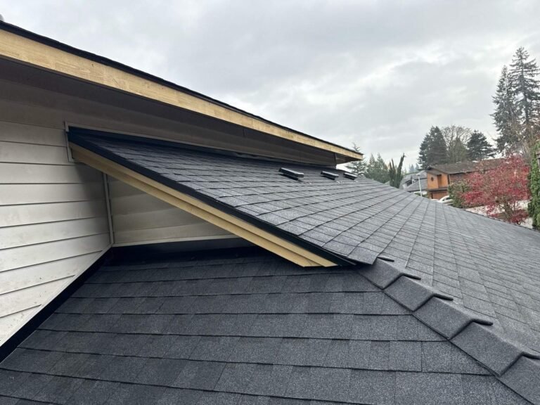 Roof slope with new gray shingles, a raised wood-trimmed gable, and hip ridge caps, under an overcast sky.