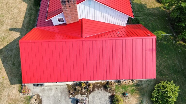 Overhead view of the red standing seam metal roof on the garage wing, with the brick chimney and upper roof above.
