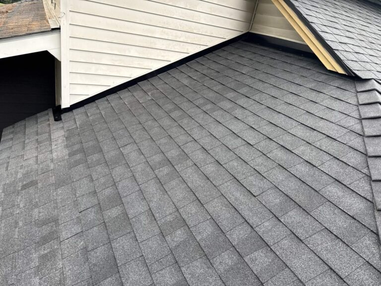 Fresh gray shingles running up to a white siding wall with a neat black flashing edge.